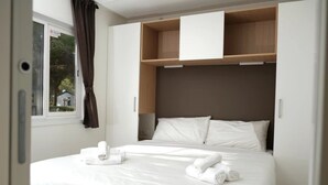 Ein ordentlich gemachtes Bett mit weißen Leinen und Handtüchern, ein hölzernes Kopfende und ein Fenster mit Vorhängen.