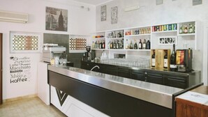Eine moderne Bar mit einer Edelstahl-Theke, Regalen voller verschiedener Flaschen und einer Wand mit Begriffen rund um Kaffee.