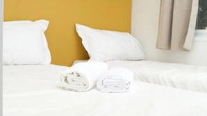 A hotel room with a yellow accent wall, white bedding, and neatly folded towels on the bed. - ZEcamping 4 étoiles pataugeoire locatif TV clim 67m2 (Alghero)