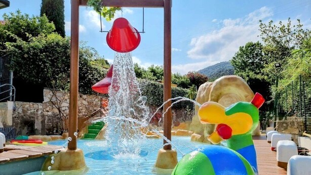 Un espace de jeux aquatiques avec une fontaine, des structures de jeu colorées et une terrasse en bois.