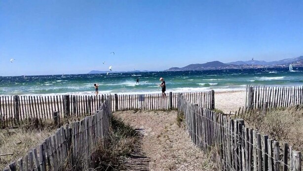 Une plage bordée d’une clôture en bois, un ciel dégagé et l’océan en arrière-plan.