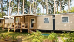 A mobile home with a porch and a small deck, surrounded by a forest.