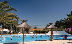 Une piscine avec des gens, des palmiers et des parasols en feuilles de palmier.