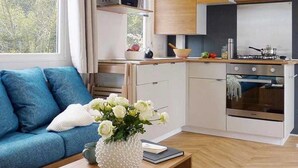 Eine moderne Küche mit Holzausbau, einer Mikrowelle und einem Backofen. Ein blaues Sofa mit weißem Kissen und ein Blumenstrauß auf einem Holztisch.
