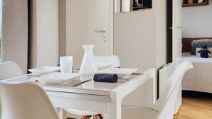 Ein modernes Hotelzimmer mit Essbereich, einem Bett mit Kopfteil und einer kleinen Regal mit Büchern.