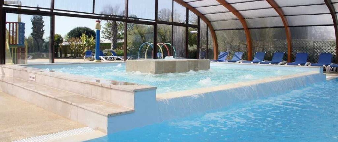 An indoor swimming pool with a water slide, lounge chairs, and a covered area.