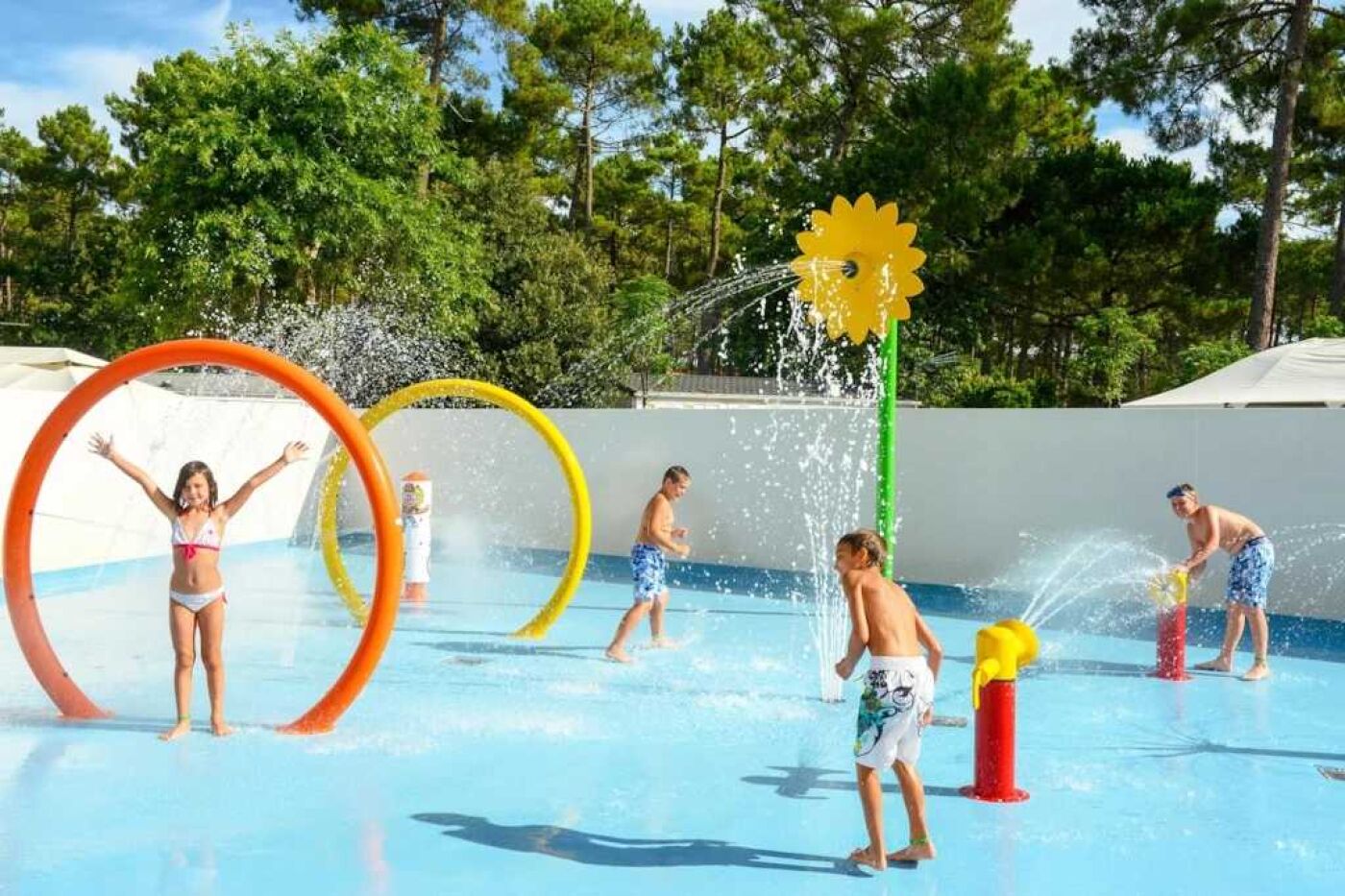 Un parc aquàtic amb nombroses instal·lacions aquàtiques, incloent anelles i un gran sortidor en forma de flor groga.
