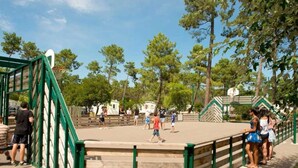 A basketball court with a green metal fence and trees in the background. - ZEcamping 4* animé espace aquatique dog friendly mobil-home 28m2 (Lège-Cap-Ferret)