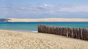 A sandy beach with a wooden fence in the foreground and a clear blue sky. - ZEcamping 4* animé espace aquatique dog friendly mobil-home 28m2 (Lège-Cap-Ferret)