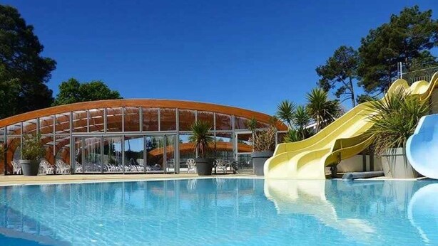 A swimming pool with a yellow slide and a glass building in the background. - ZEcamping 4* animé espace aquatique dog friendly mobil-home 28m2 (Lège-Cap-Ferret)