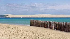 Ein sandiger Strand mit einem Holzzaun im Vordergrund und einem klaren, blauen Himmel.