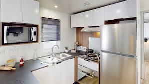 Een moderne keuken met witte kasten, roestvrijstalen apparatuur, een inbouwoven en een raam met zonwering.