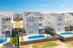 A residential area with multiple two-story houses, each featuring a front deck and a backyard with a swimming pool. - Sun Realty gorgeous Kitty Hawk home with elevator, just steps from the beach (Kitty Hawk)