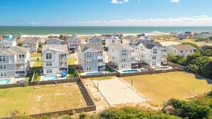 A coastal residential area with multiple two-story houses, a sandy beach, and a clear view of the ocean. - Sun Realty gorgeous Kitty Hawk home with elevator, just steps from the beach (Kitty Hawk)