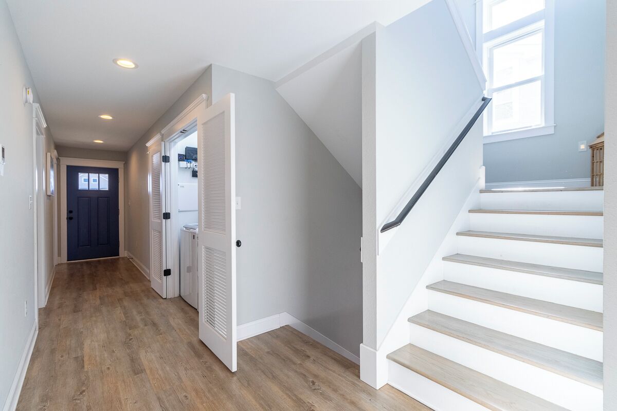 A hallway with wooden flooring, white walls, and a staircase with white steps and a gray handrail.