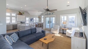 A modern living room with a dark blue sofa, a wooden coffee table, and a ceiling fan. - Sun Realty gorgeous Kitty Hawk home with elevator, just steps from the beach (Kitty Hawk)