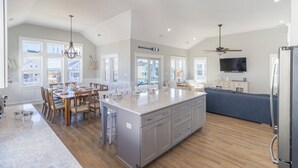 A spacious kitchen with a large island, wooden dining table, and built-in appliances. - Sun Realty gorgeous Kitty Hawk home with elevator, just steps from the beach (Kitty Hawk)