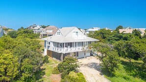 A coastal house with a large balcony, surrounded by lush greenery and other houses. - Sun Realty warm Duck NC vacation rental, just a short walk to the beach (Duck)