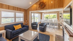 A cozy living room with a wooden ceiling, a sofa, two chairs, a coffee table, and a large window with blinds. - Sun Realty warm Duck NC vacation rental, just a short walk to the beach (Duck)