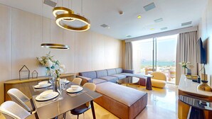 Moderni hotellihuone, jossa on ruokailutila, sohva ja suuri ikkuna, josta on näkymä.