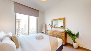 Una habitación de hotel moderna con una cama grande, un aparador de madera, un espejo y una planta en maceta.