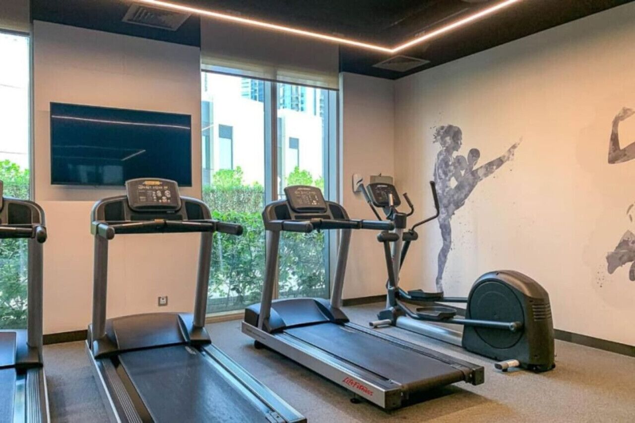 Une salle de sport équipée de tapis de course, d’un appareil elliptique et d’un mur décoré d’œuvres d’art sur le thème du fitness.