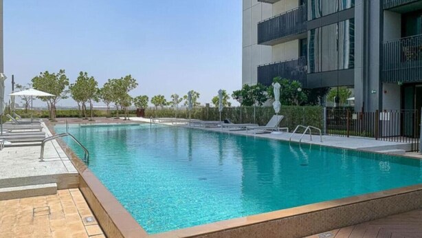 Un edificio moderno con piscina, asientos exteriores y cielo despejado.