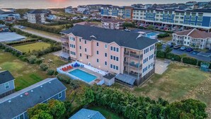 Un hôtel à plusieurs étages doté d’une piscine, situé près d’une zone côtière offrant une vue sur le coucher de soleil.