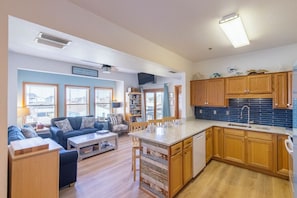 A modern kitchen with wooden cabinets, a central island, and a dining area with a sofa and coffee table.