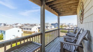 Une terrasse en bois avec des fauteuils Adirondack, une rambarde en métal et une vue sur des immeubles résidentiels.