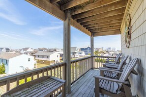 En træterrasse med Adirondack-stole, gelænder i metal og udsigt til boligbygninger.