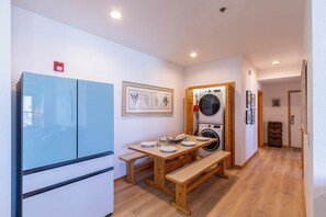 Une cuisine compacte avec un réfrigérateur bleu, une table en bois, un banc et un lave-linge.