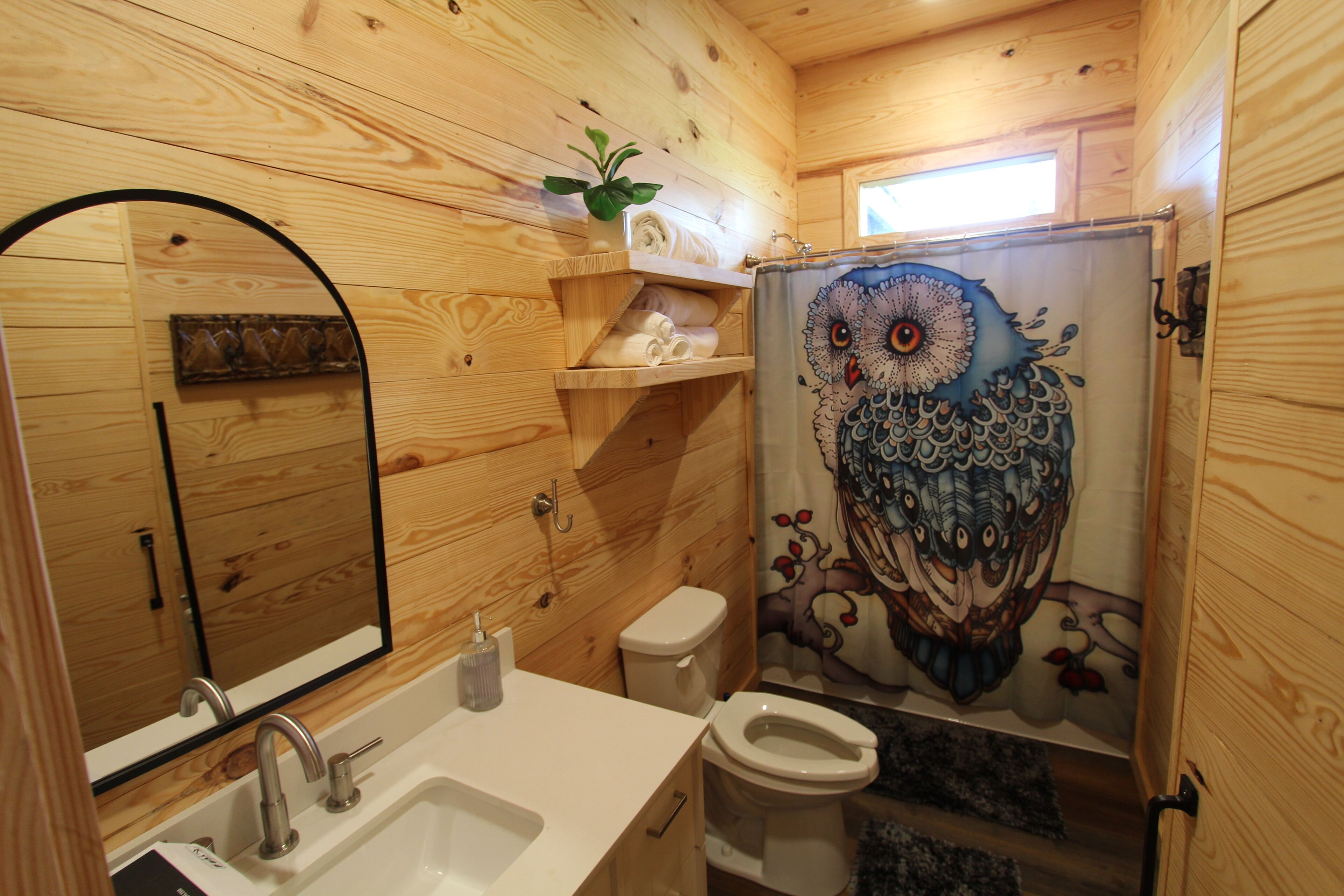 Ein Badezimmer in einer Holzhütte mit einem Holzbacheng, einer Toilette und einer Duschvorhang mit Eulenmuster.