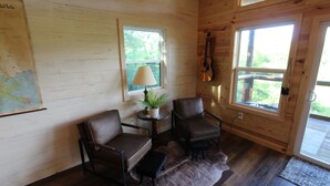 Une pièce chaleureuse aux murs en bois, avec deux fauteuils en cuir, une petite table sur laquelle se trouve une lampe, une carte accrochée au mur et une guitare suspendue au mur.