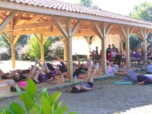 Uma área externa coberta com pessoas deitadas em tapetes, possivelmente para uma aula de exercícios em grupo ou yoga.