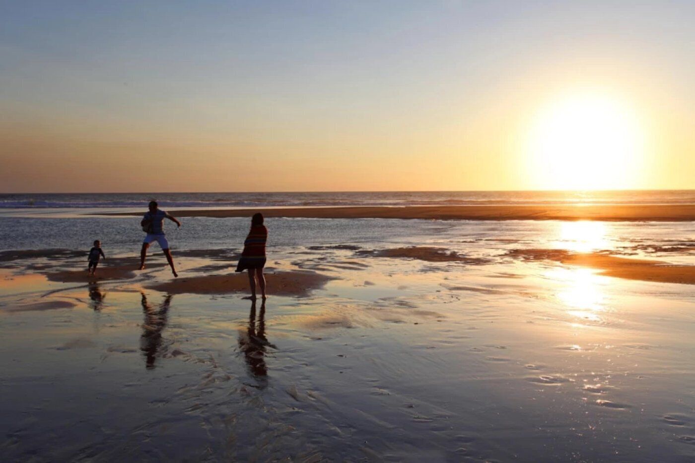 Un coucher de soleil sur la plage, avec des gens qui se promènent le long du rivage.