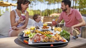A family dining outdoors with a variety of foods on a tray, including meats, vegetables, and bread. - ZEcamping 4 étoiles 500m plage espace aquatique locatif 28m2 (Seignosse)