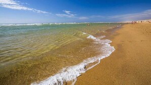 A beach with clear water, a pier in the distance, and people walking along the shore. - ZEcamping 4* animé 500m plage espace aquatique locatif TV LV clim 36m2 (Seignosse)