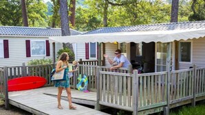 A wooden deck leading to a covered porch with a view of a house in the background. - ZEcamping 4* animé 500m plage espace aquatique locatif TV LV clim 36m2 (Seignosse)