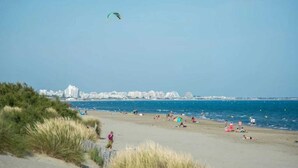 Una playa con gente, césped y edificios al fondo.