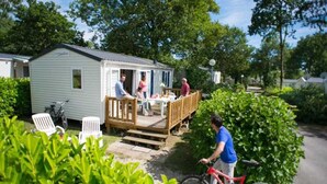 A mobile home with a porch and a table where people are seated. - ZEcamping 4* piscine couverte toboggans locatif 28m2 6 pers (Névez)