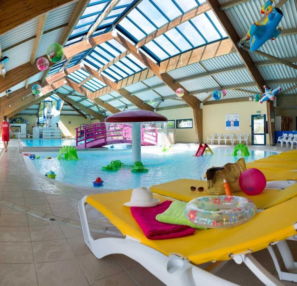Una piscina interior con toboganes, zona de juegos acuáticos y sillones de relax.