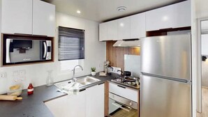 Una cocina moderna con armarios blancos, electrodomésticos de acero inoxidable, horno empotrado y ventana con persianas.