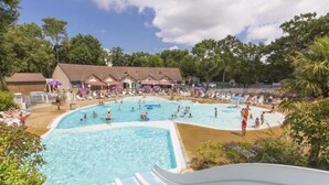 Una gran piscina al aire libre rodeada de sillones de descanso y sombrillas, con un edificio al fondo.