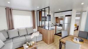 Una sala moderna con un sofá, una mesa de centro y un comedor con mesa y sillas. Se observa una zona de cocina con refrigerador y estufa.