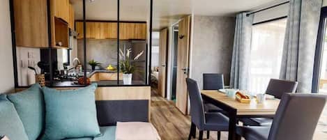 A modern living room with a sofa, dining table, chairs, and a kitchen area visible through a glass partition.