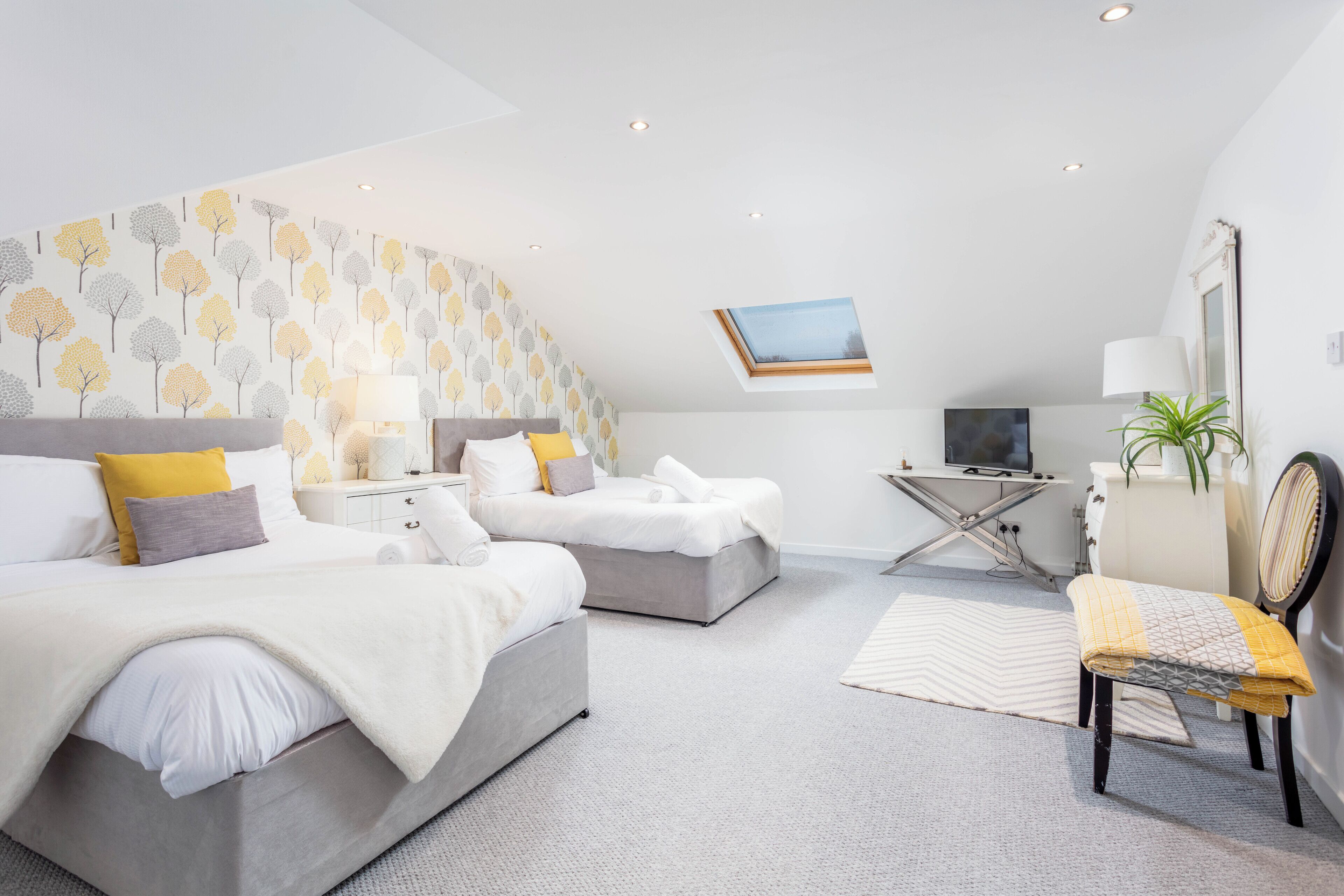 A modern bedroom with two beds, a desk, and a chair.