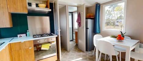 A compact kitchen with a gas stove, a refrigerator, and a dining area with a table and chairs.