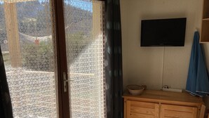 Una stanza con un armadio in legno, una televisione fissata al muro e una porta vetrata scorrevole con tenda decorata.