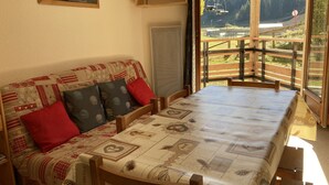 Una stanza accogliente con un divano in legno e un tavolo, una finestra con vista su una montagna e una seggiovia, e un quadro appeso al muro.